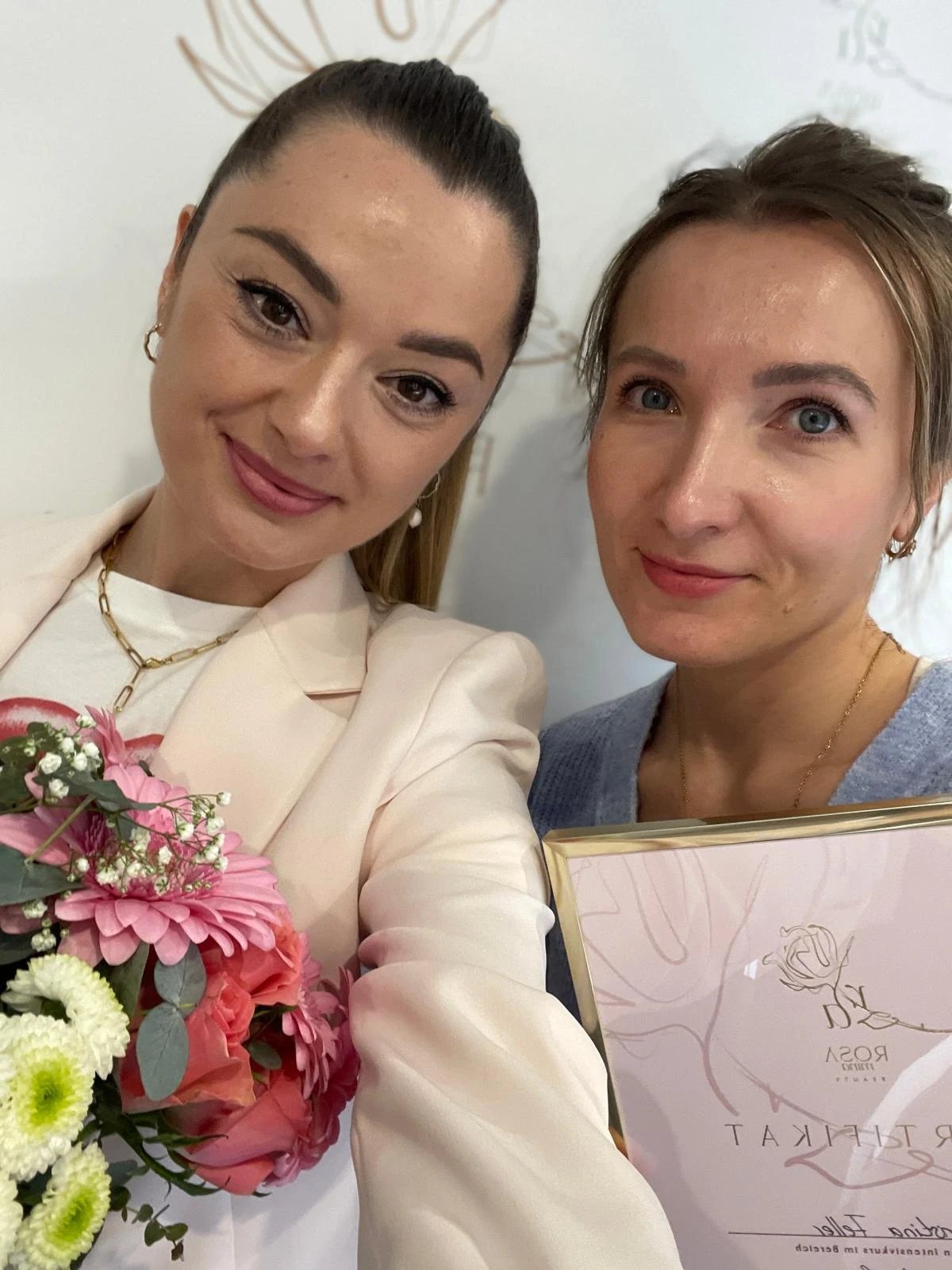 Zwei Frauen mit Zertifikat und Blumenstrauß.